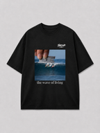 Zwart oversized THE WAVE OF LIVING T-shirt van FAKESNIFF, print 'the wave of living': een hand houdt een scheermesje boven een golf waarop drie surfers rijden