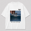 Wit oversized THE WAVE OF LIVING T-shirt van FAKESNIFF, print 'the wave of living': een hand houdt een scheermesje boven een golf waarop drie surfers rijden