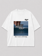 Wit oversized THE WAVE OF LIVING T-shirt van FAKESNIFF, print 'the wave of living': een hand houdt een scheermesje boven een golf waarop drie surfers rijden